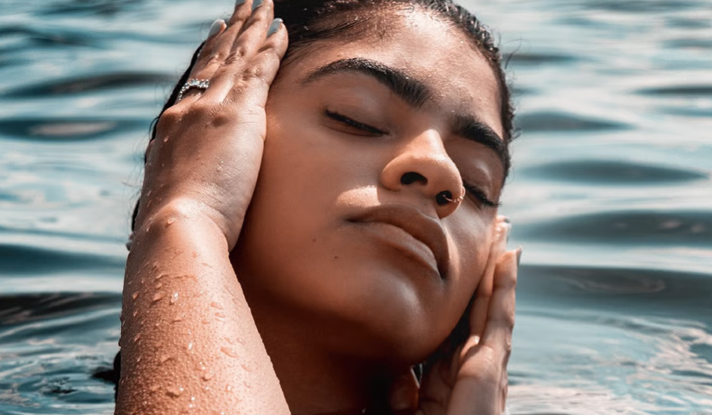 Woman in water with eyes closed, hands to her ears