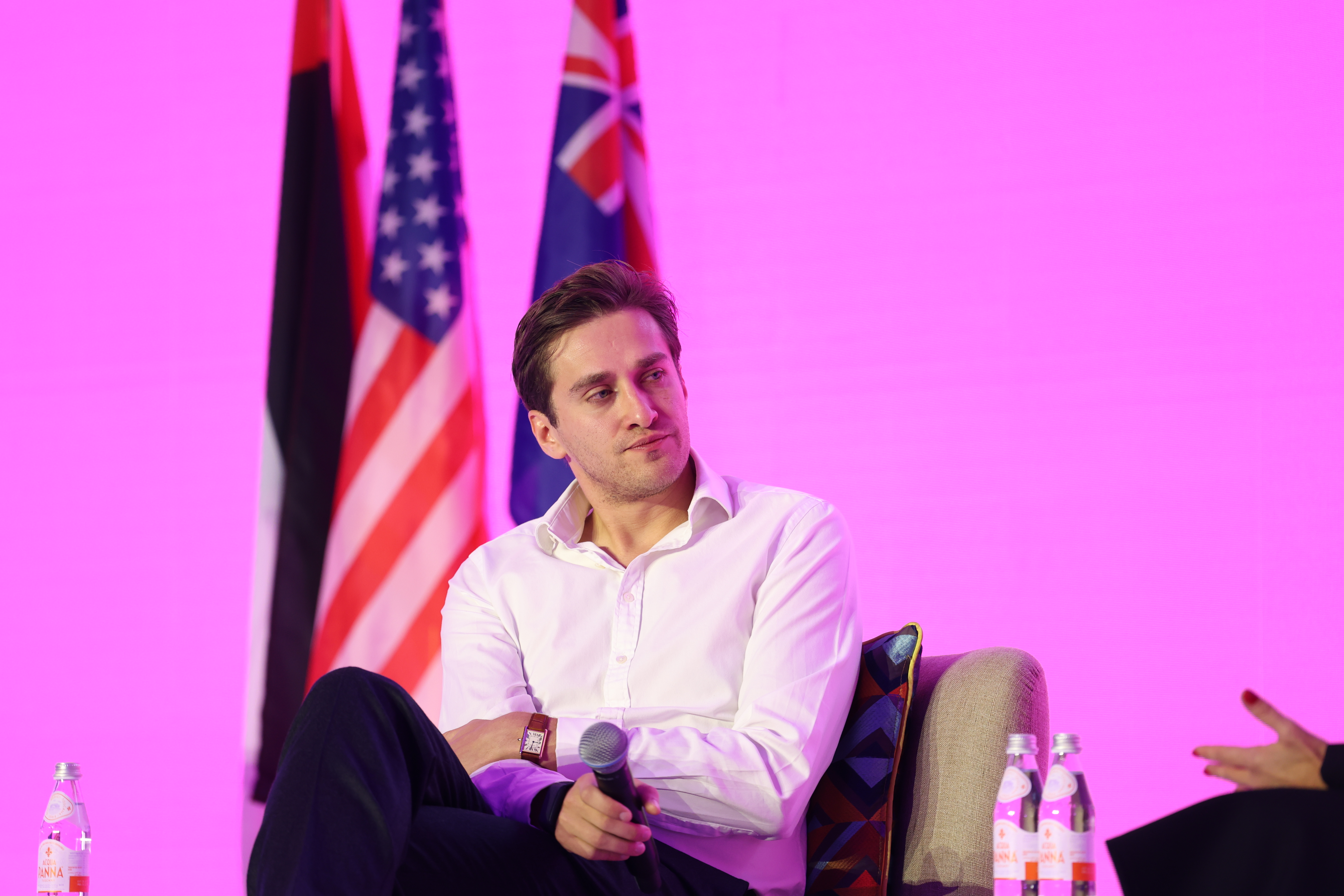 Man in a white shirt seated on a conference panel beside international flags