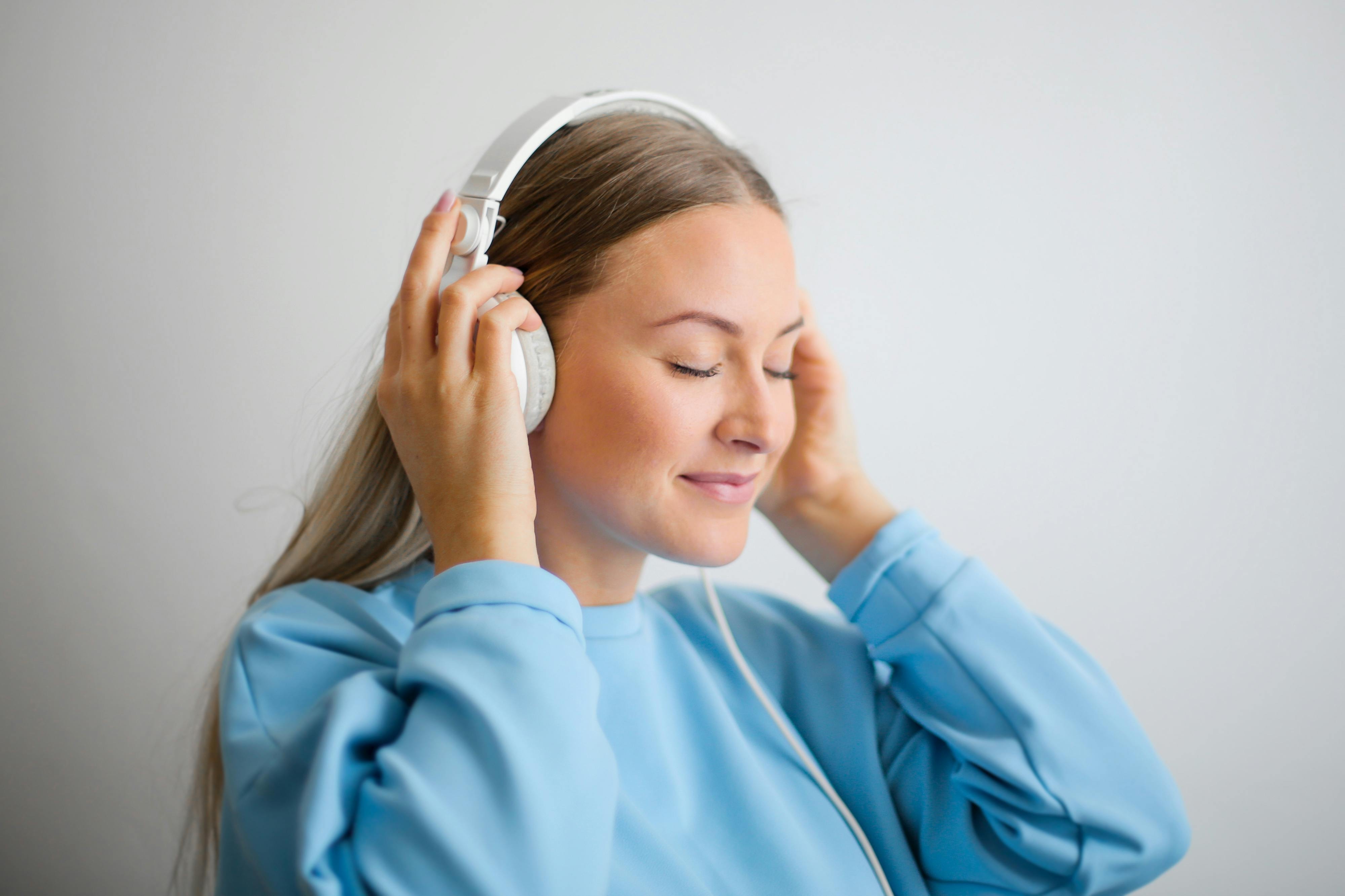 Woman in a blue jumper listening with white headphones